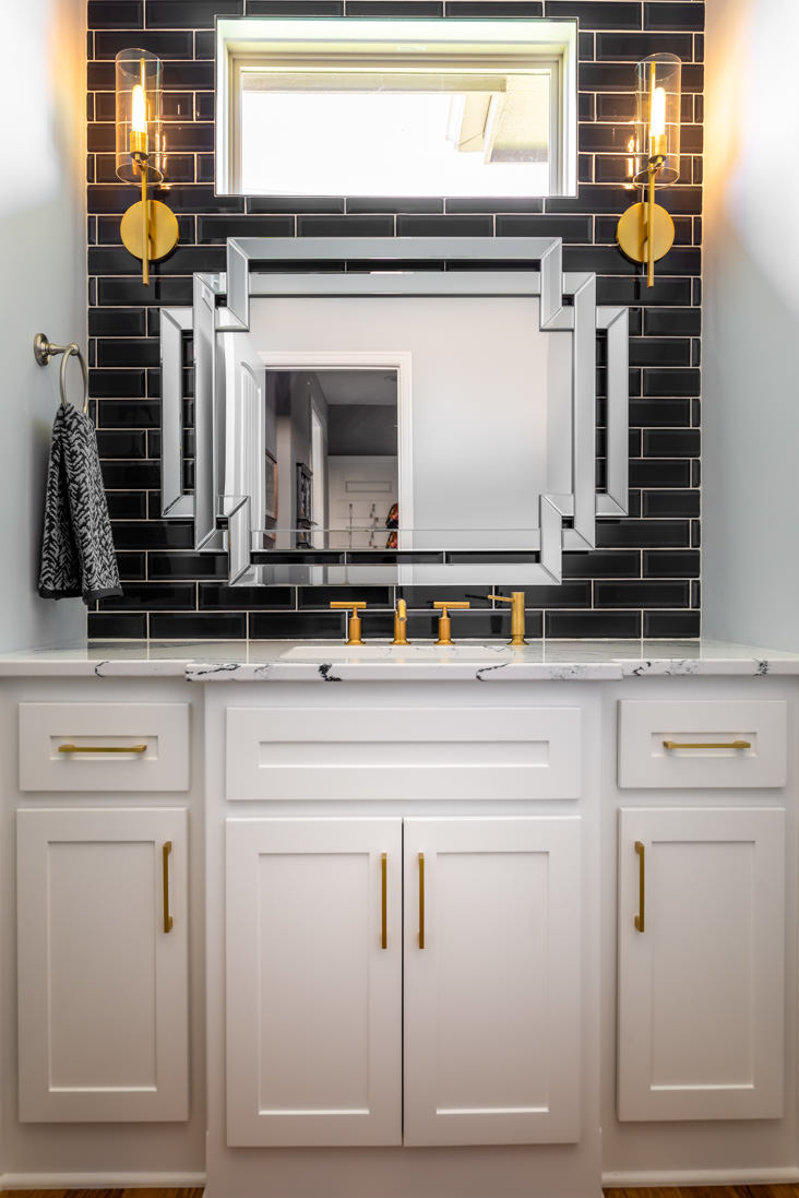 A charming powder room with contrasting black tiles and brass fixures
